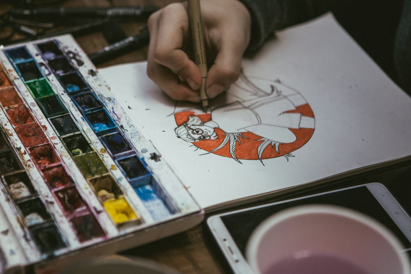 画用紙の近くで絵の具の近くでスケッチブックにアニメキャラクターを描くアーティスト。