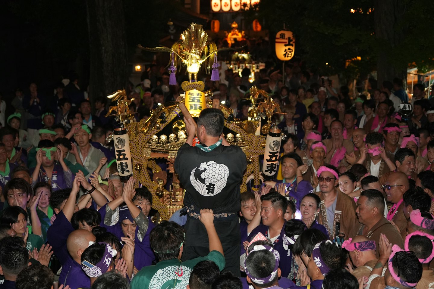 人が混雑した祭りで金色の神輿を誘導している。