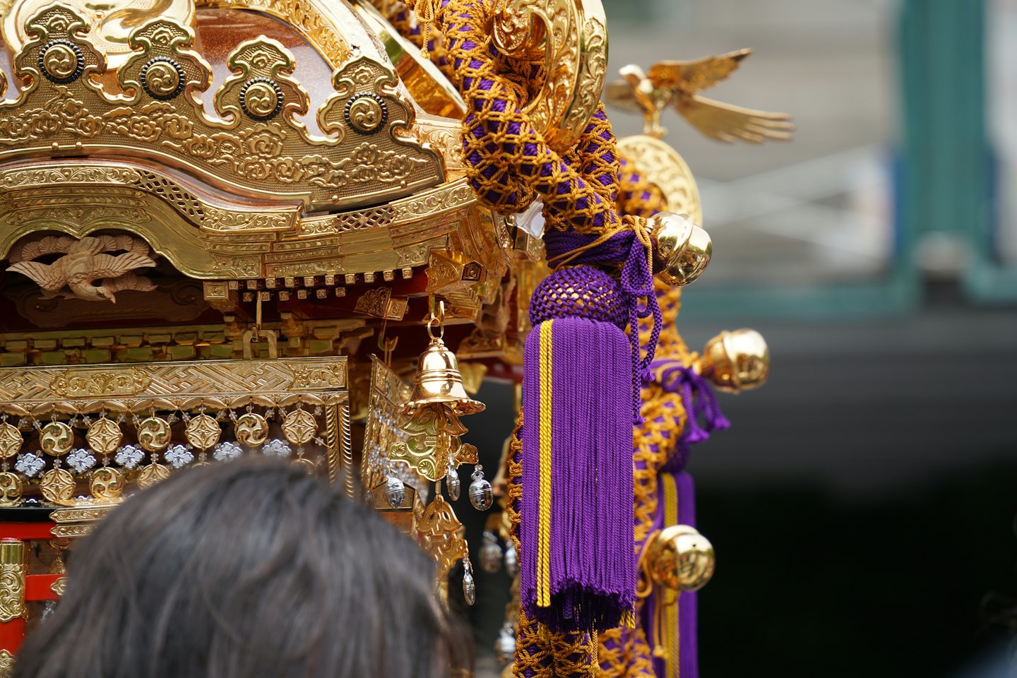 精巧な金の彫刻と紫の房飾りが伝統的な祭りの山車を飾っています。